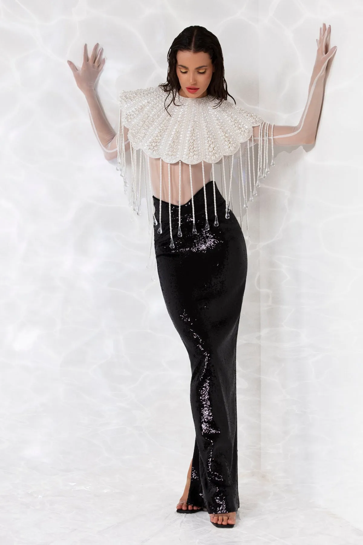 Scallop shell inspired ensemble consisting of a cropped top embroidered with pearls, crystals, and hand blown glass drops. Worn with a white sheer bodysuit and a pencil skirt in high gloss sequins